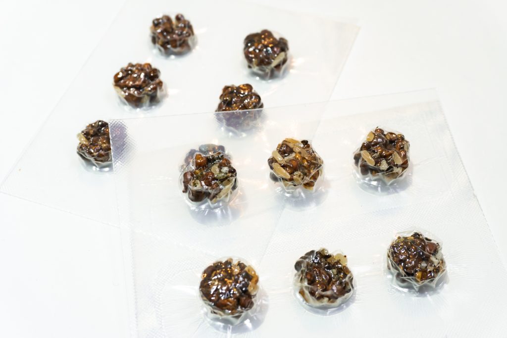 Small, round confections with a glossy, dark coating, scattered on clear plastic sheets.