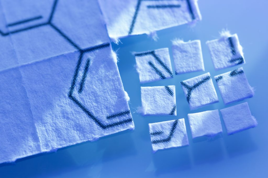 Small squares of paper with chemical structure patterns, arranged on a reflective blue surface.