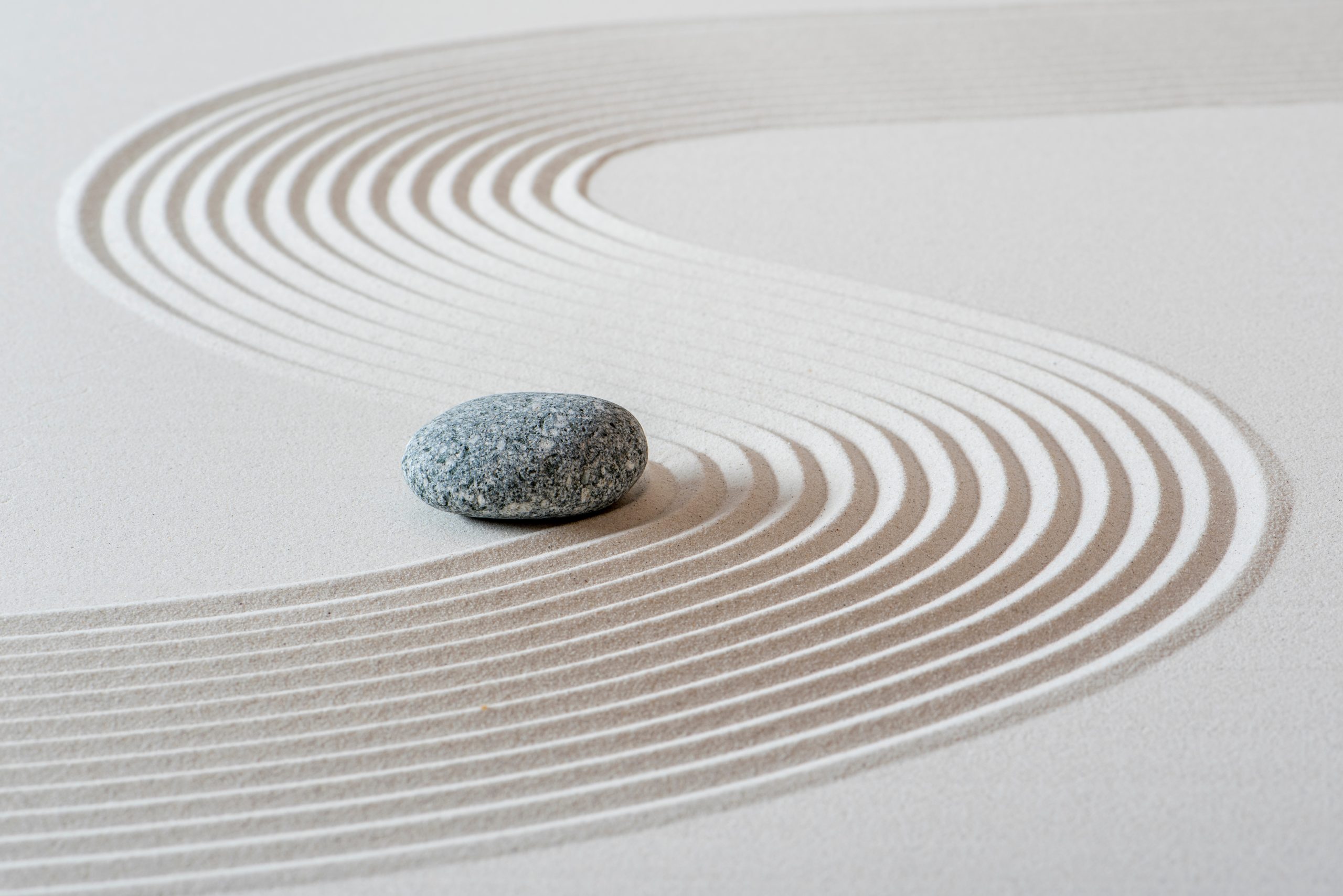 A smooth stone rests on a bed of white sand, with gentle, curved lines etched into the surface around it.