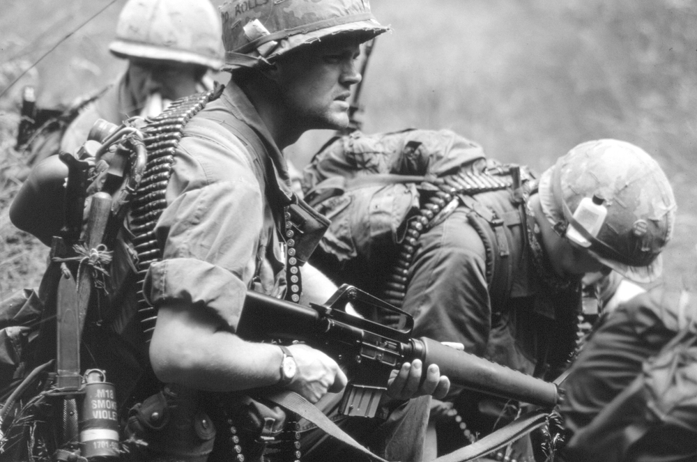 Soldiers in military gear, armed and focused, navigate a dense, grassy terrain during a tense moment.