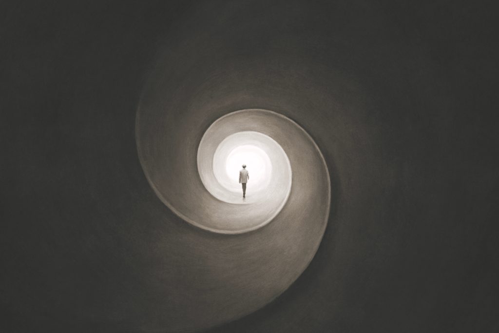A solitary figure walks through a spiraling tunnel, illuminated by a bright light at the end.