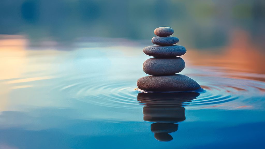Stack of smooth stones balanced on water, creating gentle ripples, with a soft, blurred background.