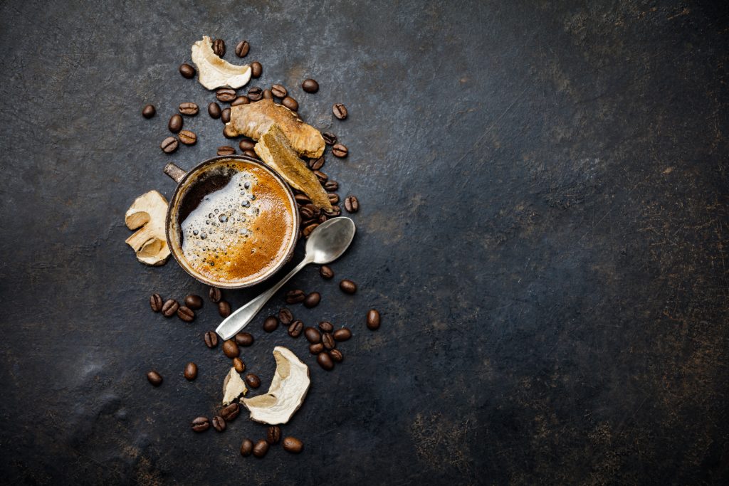 A steaming cup of coffee surrounded by coffee beans and dried fruit slices on a dark textured surface.