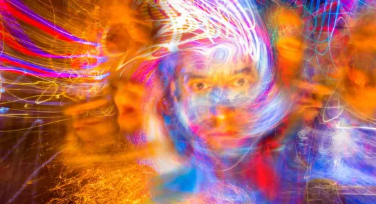 Swirling colors and lights create an abstract, dreamlike portrait with a central face surrounded by vibrant patterns.
