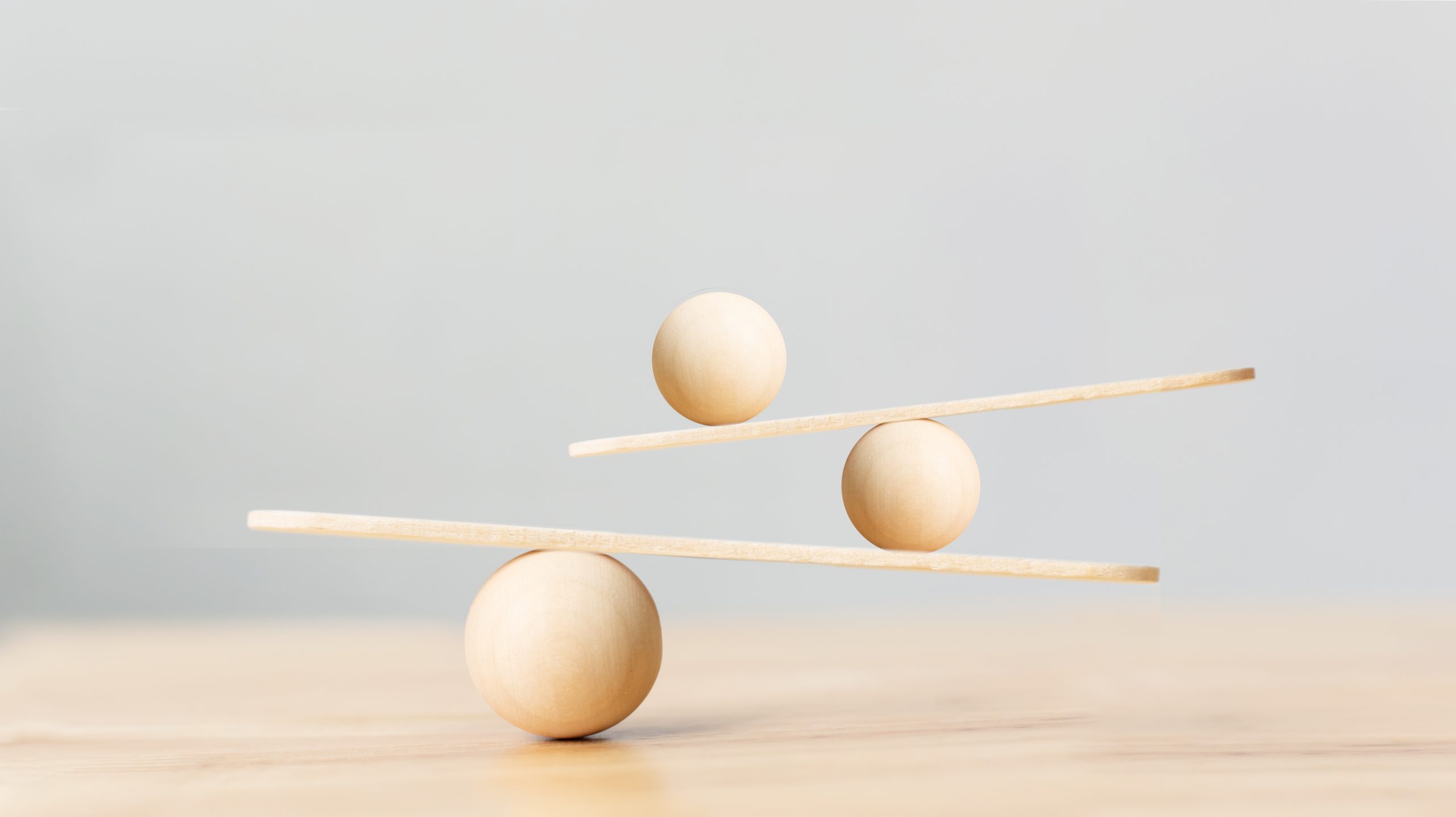 Three wooden spheres balanced on two horizontal sticks against a soft gray background.