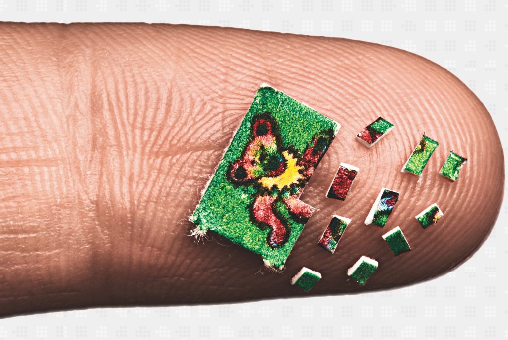 A tiny, colorful butterfly painted on a miniature canvas rests on a fingertip, surrounded by smaller fragments.