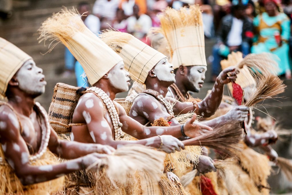 Traditional dancers in elaborate headdresses and body paint perform with enthusiasm, surrounded by a vibrant audience.