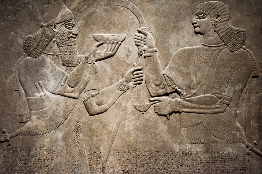 Two ancient figures in relief, one holding a bowl and the other wielding a sword, set against a textured stone background.