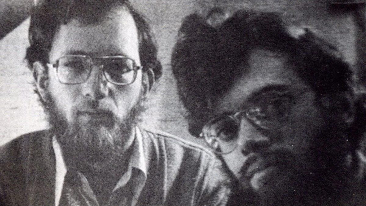 Two bearded men wearing glasses, looking directly at the camera with serious expressions. Black and white photo.