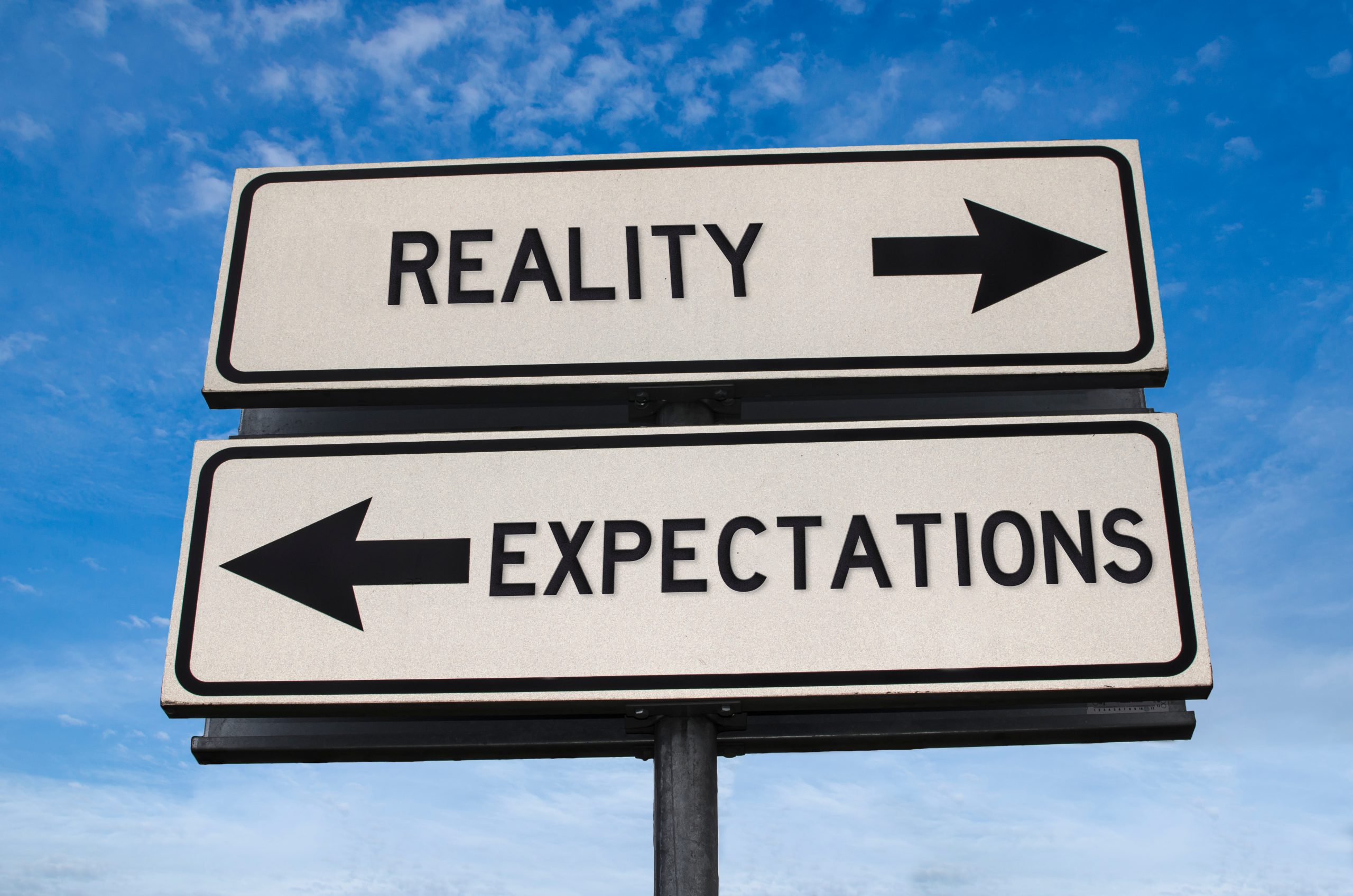 Two directional signs labeled "Reality" pointing right and "Expectations" pointing left against a blue sky.
