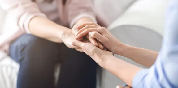 Two hands clasped together, conveying support and connection, with a soft, blurred background.