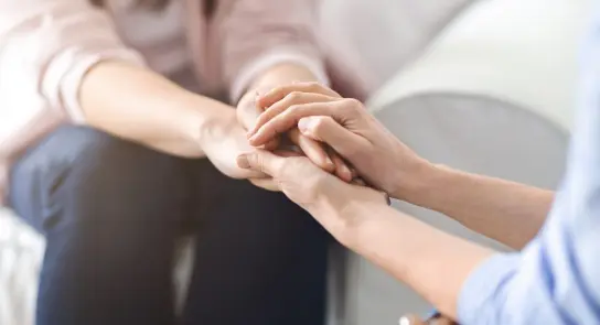 Two hands clasped together, conveying support and connection, with a soft, blurred background.