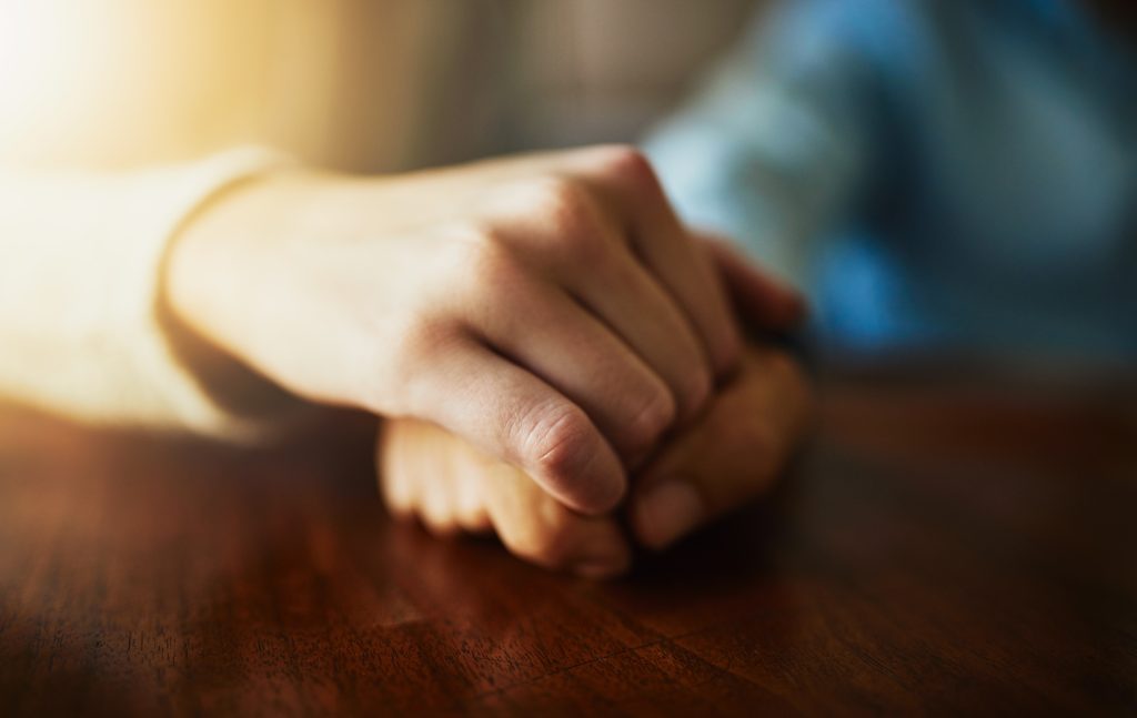 Two hands clasped together on a wooden table, symbolizing connection and support. Soft light enhances the warmth.