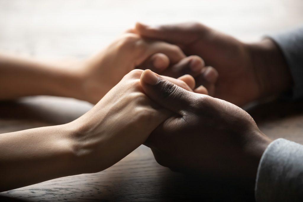 Two hands, one light and one dark, gently clasped together on a wooden surface, symbolizing connection and support.