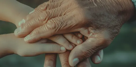 Two pairs of hands, one small and smooth, the other large and weathered, gently overlapping in a tender gesture.