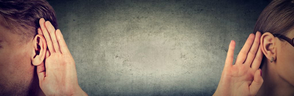 Two people with hands cupped to their ears, facing away from each other against a textured gray background.