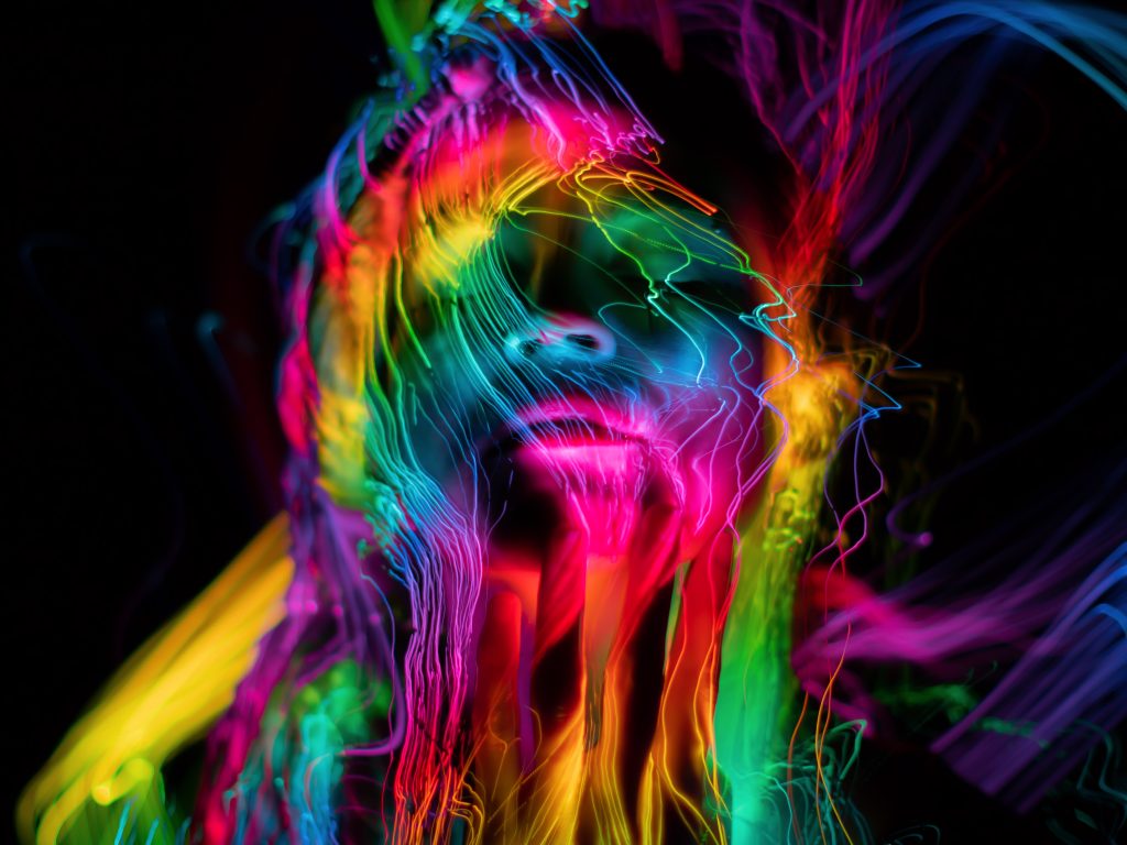 A vibrant, abstract portrait with swirling neon colors illuminating a face against a dark background.