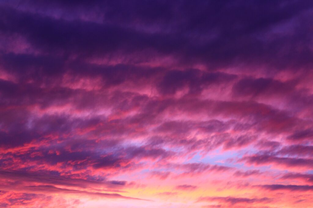 Vibrant purple and pink clouds swirl across the sky at sunset, creating a dramatic and colorful atmosphere.