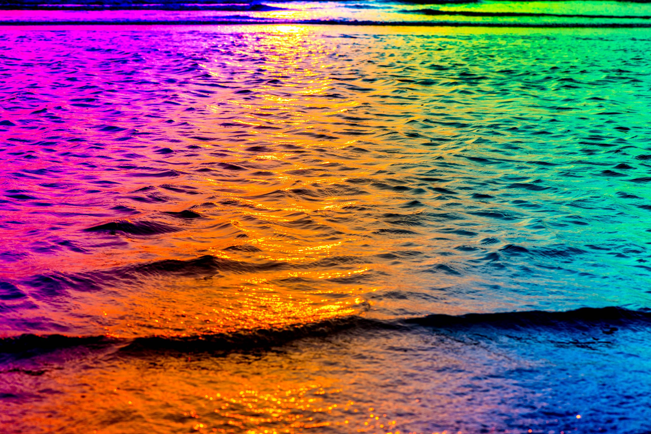 Vibrant rainbow hues reflect on gentle ocean waves, creating a mesmerizing, colorful seascape.