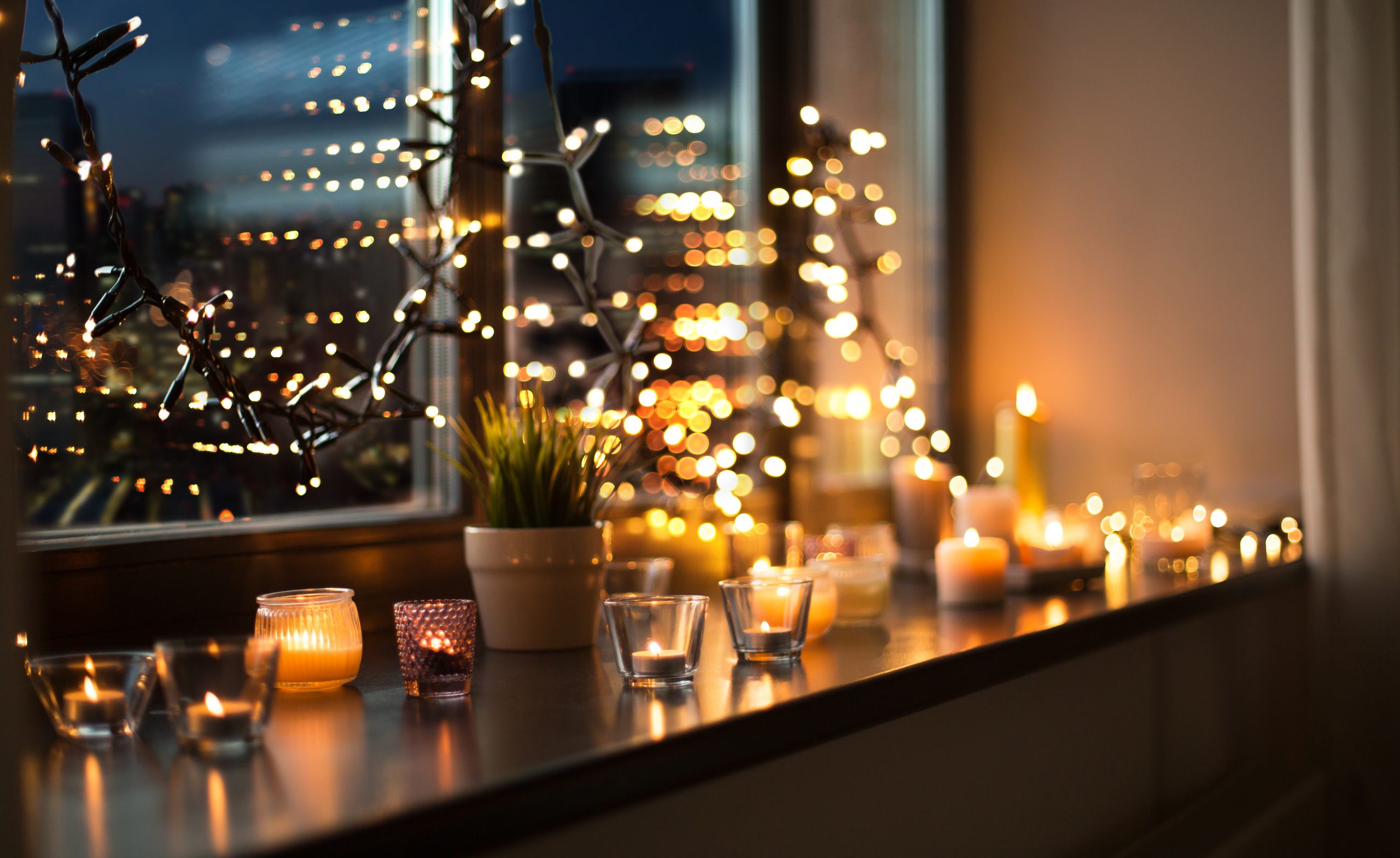 Warm candlelight and twinkling fairy lights illuminate a cozy windowsill, creating a serene evening ambiance.
