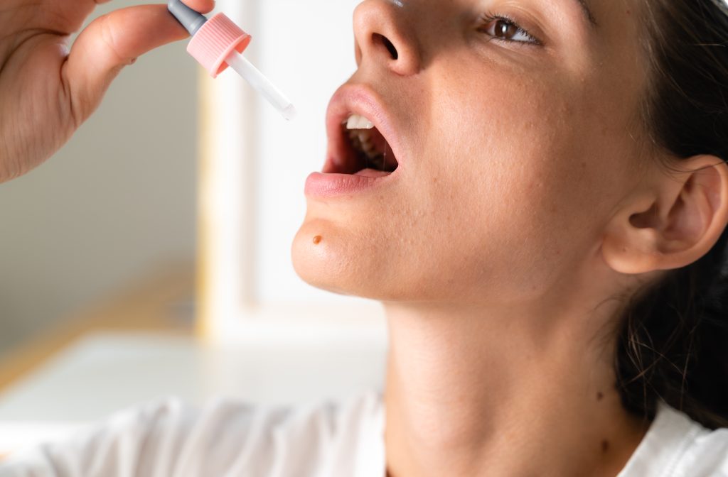 Woman administering liquid from a dropper into her open mouth, focused expression, soft lighting.