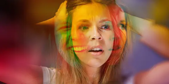 A woman with a distressed expression holds her head, overlaid with vibrant, colorful facial expressions.