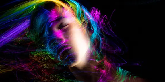 A woman with flowing hair surrounded by vibrant, swirling neon lights against a dark background.