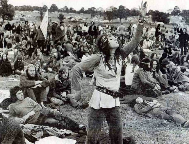 A woman in a flowing outfit dances joyfully at a crowded outdoor festival, surrounded by seated attendees.