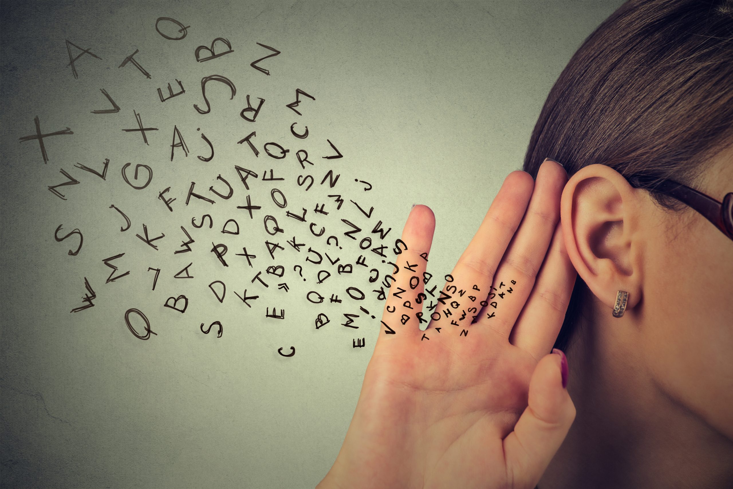 A woman with glasses holds her hand to her ear, as letters swirl around her, symbolizing listening and communication.