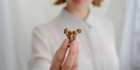 A woman in a light blouse holds a cluster of small, brown mushrooms between her fingers.