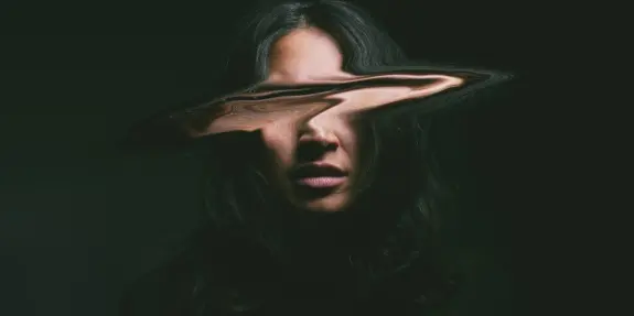 A woman with long, dark hair and a distorted face, set against a dark background, creating an eerie, surreal effect.