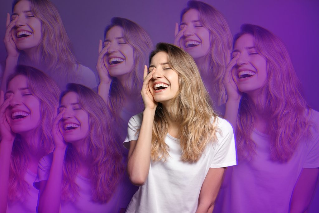 A woman with long, wavy hair laughs joyfully, surrounded by a vibrant purple and pink background.