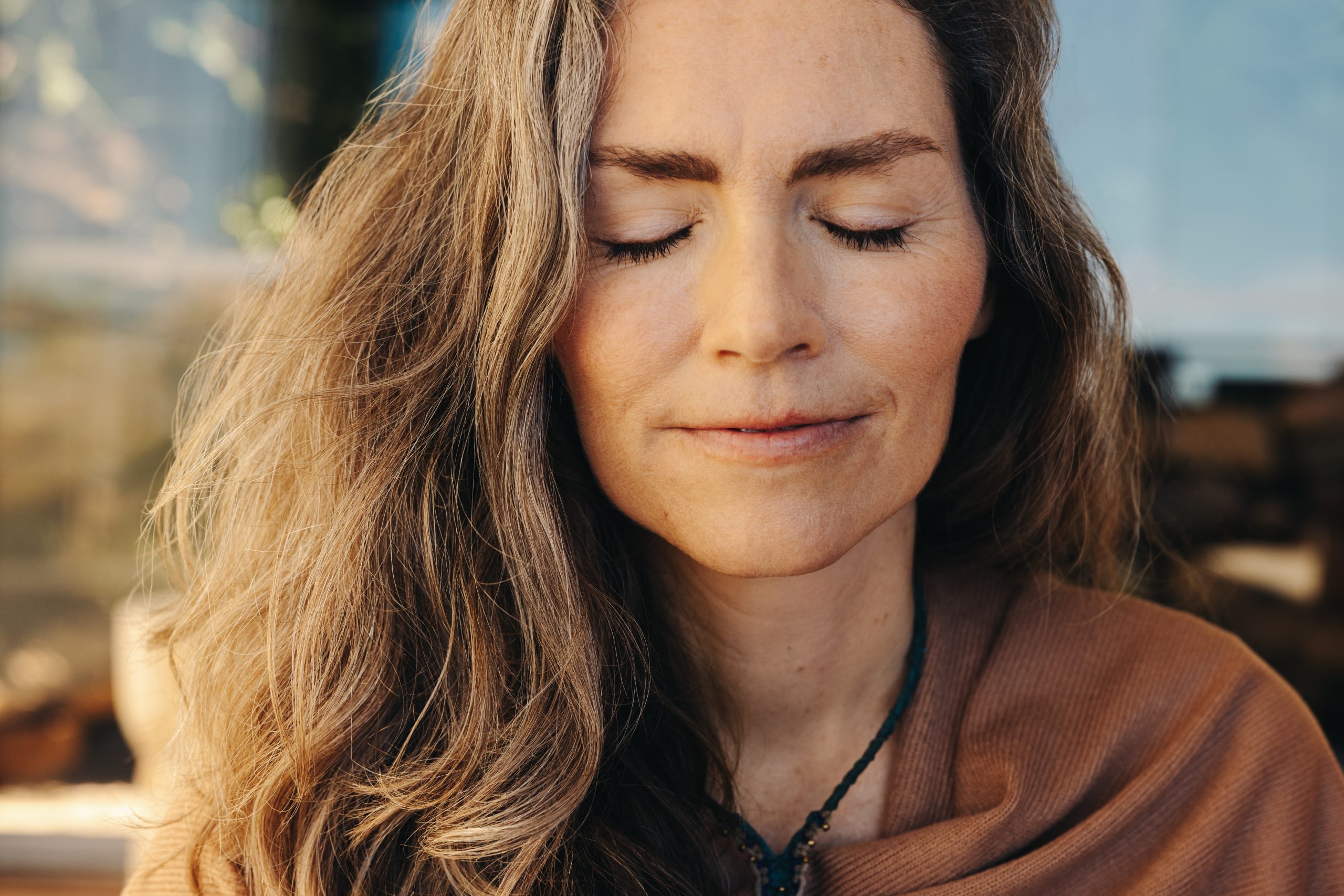 Woman with long, wavy hair and closed eyes, exuding calmness and serenity, wearing a brown shawl.