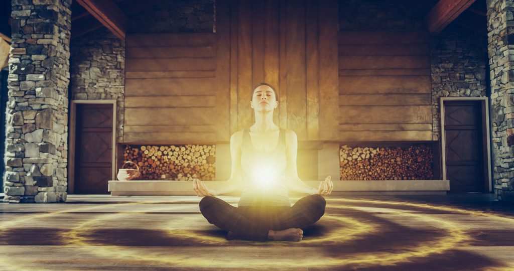 A woman meditates in a serene stone room, radiating light from her heart, surrounded by a glowing circle.