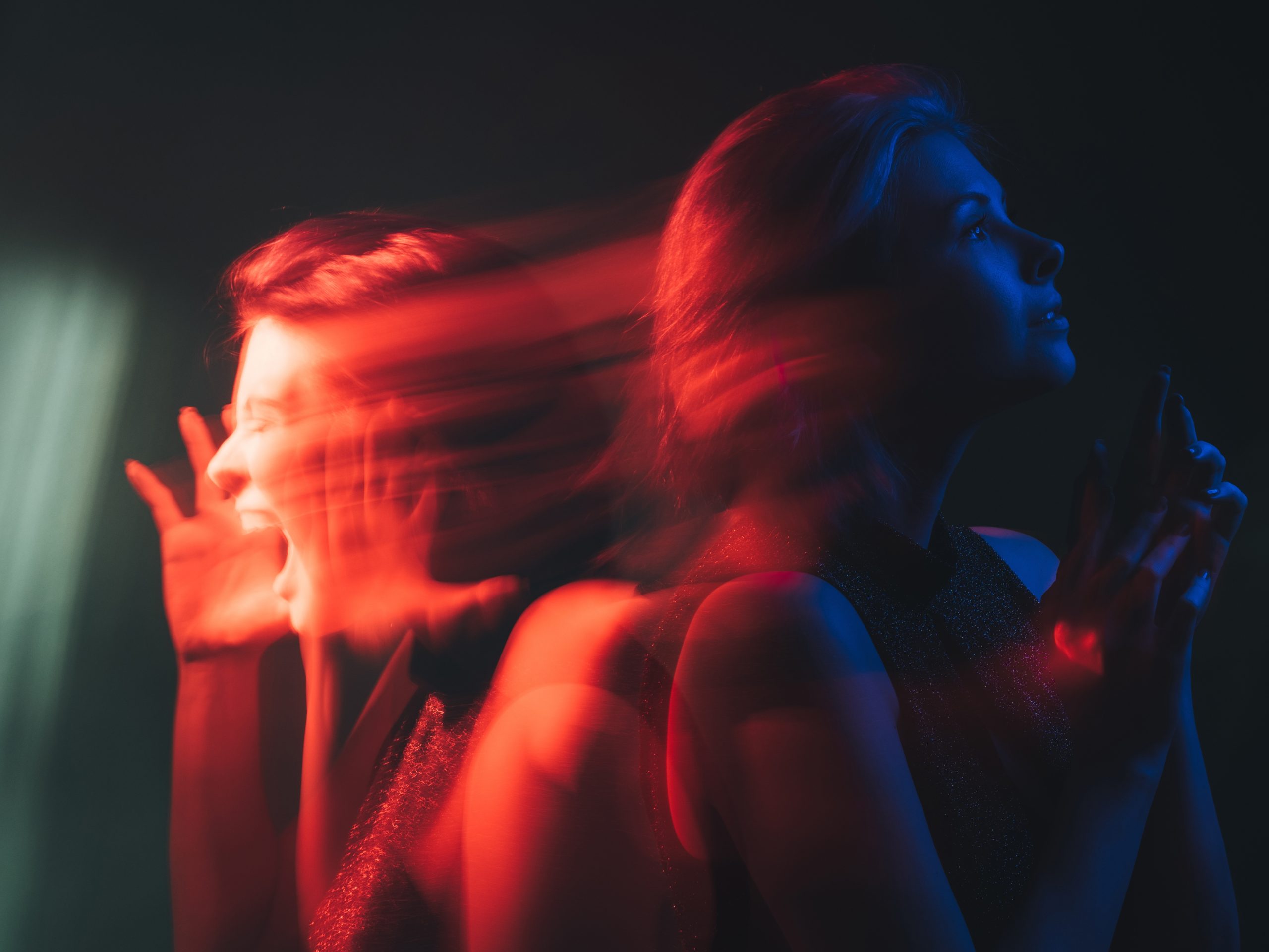 A woman in profile with a serene expression, contrasted by a blurred figure screaming, illuminated in red and blue light.