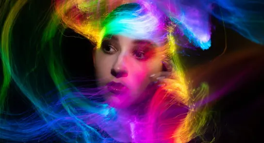 A woman with vibrant, swirling neon colors around her face, creating a dynamic and ethereal atmosphere.