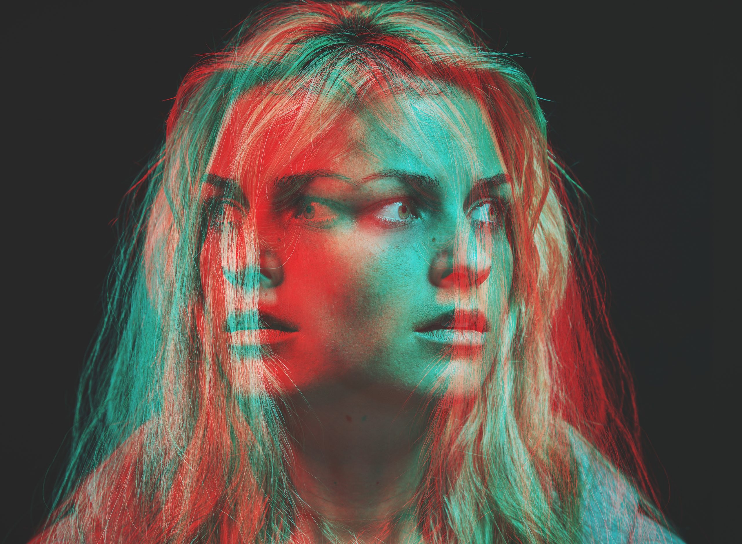 A woman with wavy blonde hair, her face appearing in a surreal, double-exposed effect with red and teal hues.