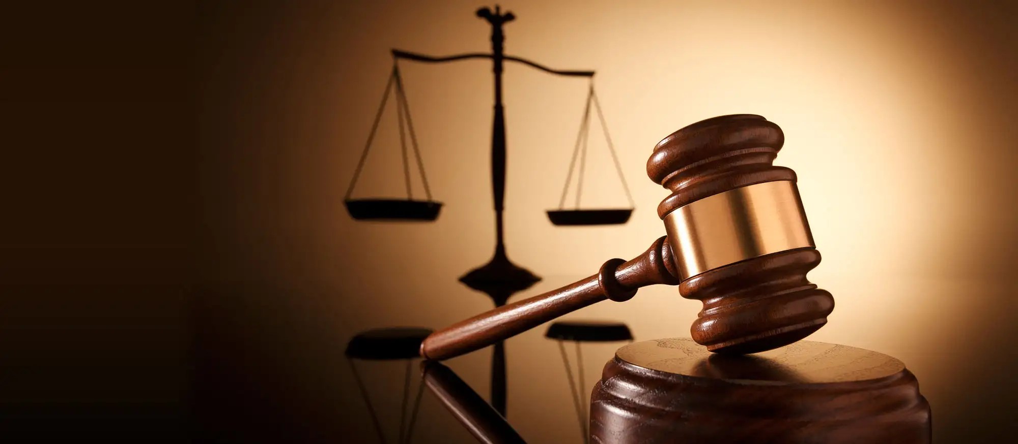 Wooden gavel in the foreground with a blurred scale of justice in the background, symbolizing law and order.