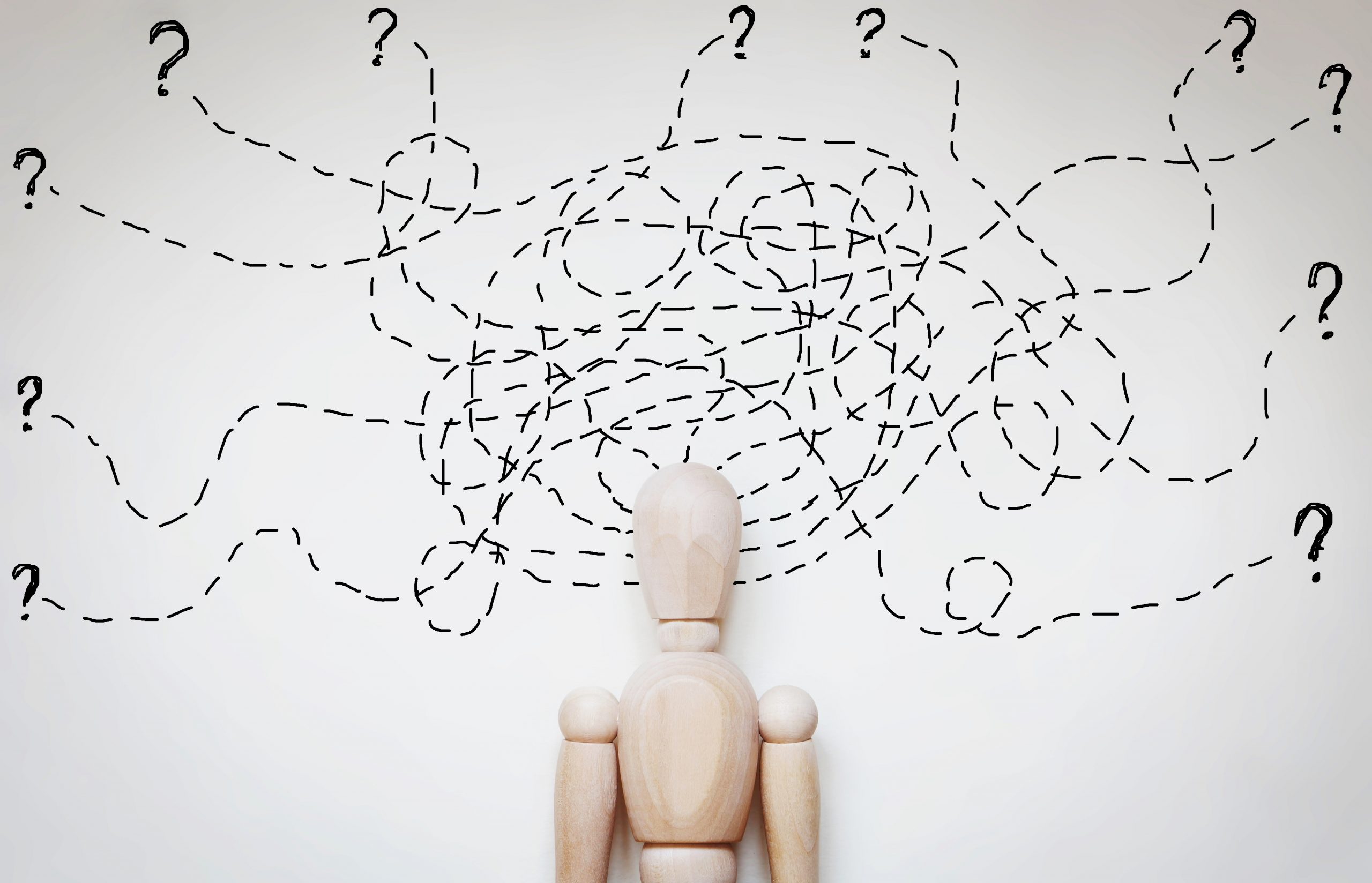 A wooden mannequin stands before a wall filled with chaotic, dashed lines and question marks, symbolizing confusion.