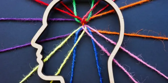 Wooden silhouette of a head with colorful threads radiating outward, symbolizing creativity and mental connections.