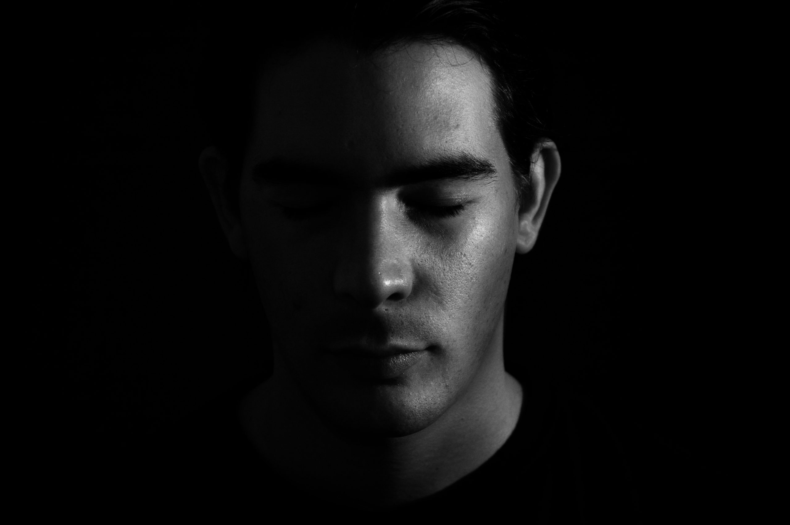 A young man with closed eyes, half his face illuminated, the other half in shadow, creating a dramatic contrast.